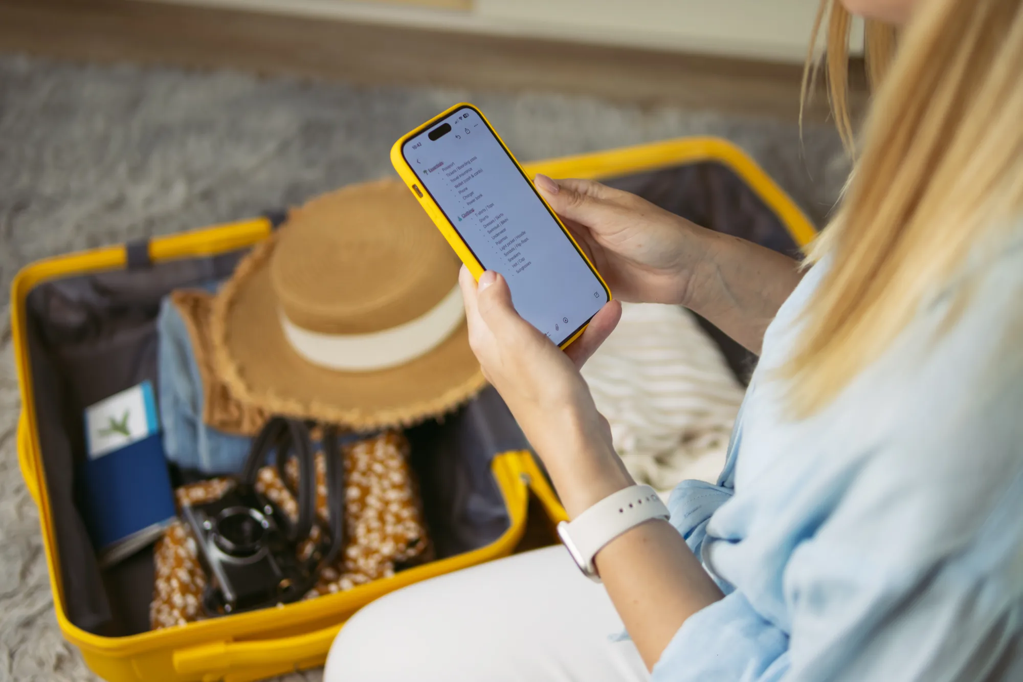 スーツケースの前でスマートフォンを見ながら旅の準備をする様子